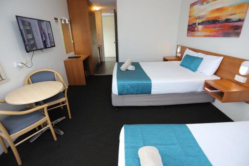 a hotel room with two beds and a desk and a chair at Citigate Motel Newcastle in Newcastle