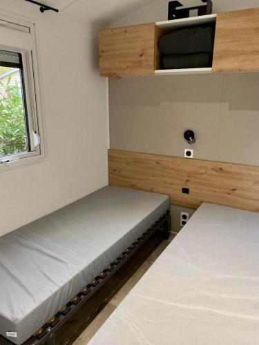 deux lits dans une petite pièce avec une fenêtre dans l'établissement MOBIL-HOME 3CH 34 m2 à SAINT-CYPRIEN, à Saint-Cyprien