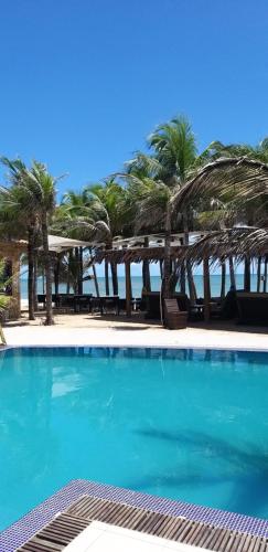 a blue swimming pool with palm trees and the ocean at ALIZE CUMBUCO in Cumbuco