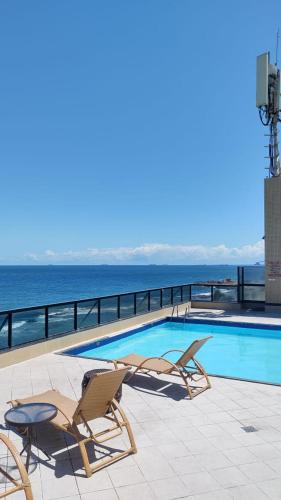 a swimming pool with two lounge chairs and the ocean at Apartamento Farol Barra Flat in Salvador