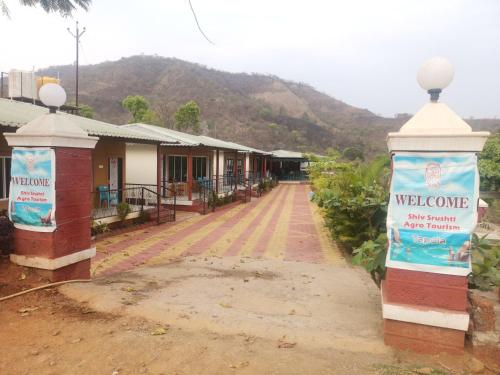 eine Straße mit einem Willkommensschild vor einem Gebäude in der Unterkunft Shivshrushti Agro Tourism & River Camp Tapola in Mahabaleshwar