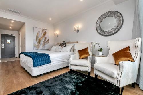 a bedroom with a bed and two chairs and a mirror at Sky Tower Serenity + Rooftop Pool in Auckland