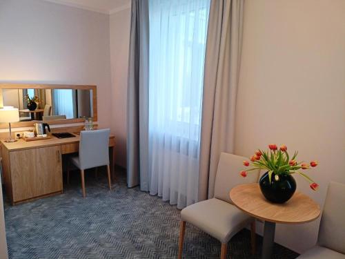 a hotel room with a desk and a table with a vase of flowers at Hotel Gromada in Koszalin