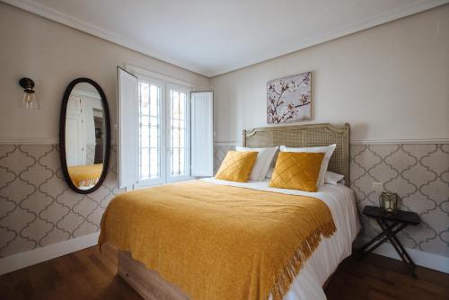 1 dormitorio con 1 cama con manta amarilla y espejo en Magno Apartments Vidrio, en Sevilla