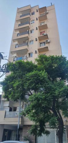 un edificio alto con un árbol delante de él en Departamento de 2 dormitorios con asador en Santiago del Estero