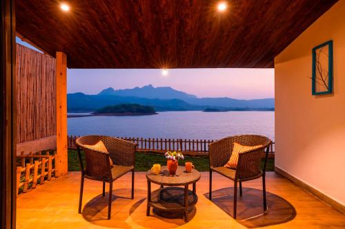 a porch with two chairs and a table with a view of the water at Zostel Plus Lonavala in Lonavala