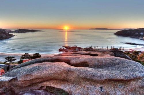 a sunset over the ocean with a large rock at Apartamento Chamela in O Pindo