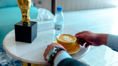 een persoon met een kopje koffie en een fles water bij فندق ارجان بارك Arjan Park Hotel in Wadi ad-Dawasir