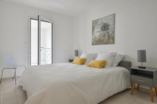 - une chambre blanche avec un grand lit blanc et des oreillers jaunes dans l'établissement T2 NEUF B4 RDJ - PISCINE–ACCÈS DIRECT PLAGES ET CENTRE VILLAGE -, à Saint-Cyr-sur-Mer