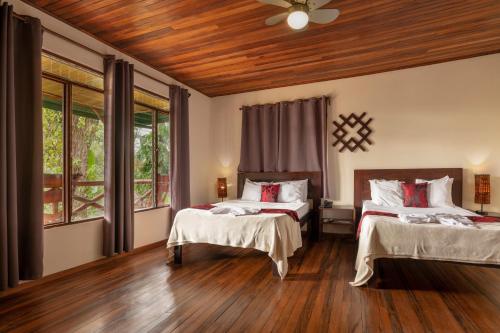 two beds in a room with wood floors and windows at Tabulia Tree in Manuel Antonio