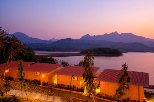 a row of houses on the shore of a lake at sunset at Zostel Plus Lonavala in Lonavala