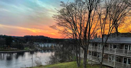 a sunset over a river with a house and trees at Inn at the Falls in Bracebridge