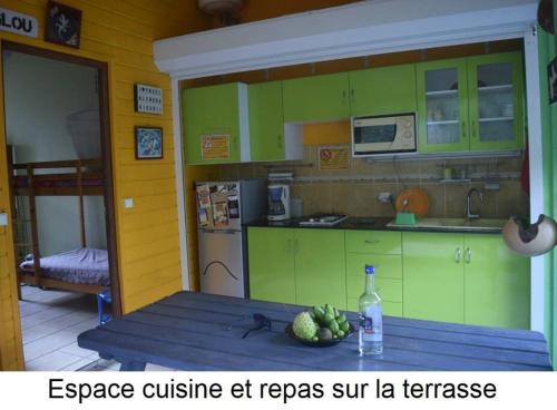 een keuken met groene kasten en een tafel met een fles water bij Gite à 2 pas de la flamboyante plage de La Perle in Deshaies