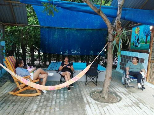 three women sitting in chairs in a hammock under a tree at Finca Ecoturistica LOS JAGUEYES in Baraya