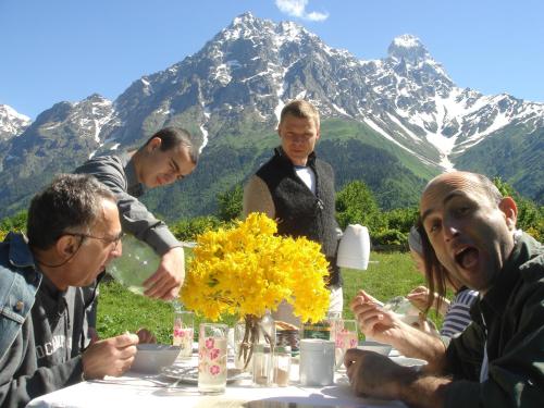 a group of people sitting at a table with mountains in the background at Grand Hotel Ushba in Mazeri