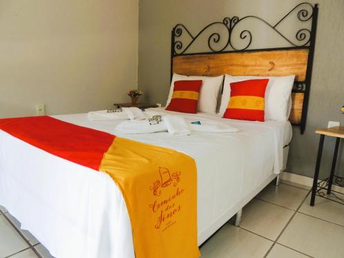 蒂拉登特斯Pousada Caminho Dos Sinos的一间卧室配有红色和黄色枕头的床