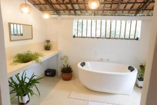 a bathroom with a large white tub and plants at Casa Alegre Trancoso, piscina, 3 suítes e ar-cond. in Trancoso