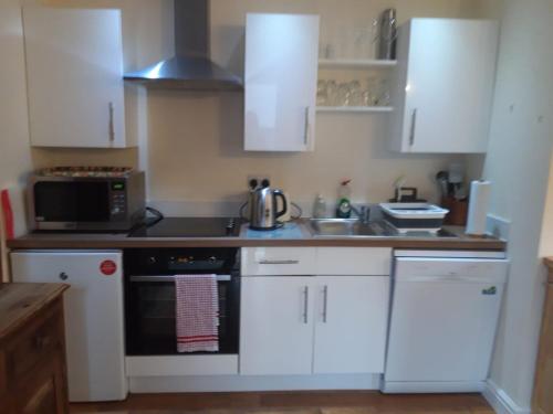 uma cozinha com armários brancos e um forno de fogão preto em Little Orchard Cottage em Canterbury