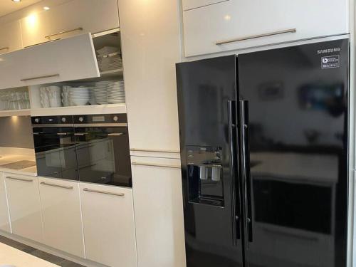 a black refrigerator in a kitchen with white cabinets at Luxury Portrush Holiday Homes - The Glynn, Portrush Sleeps 12 - 5 bedrooms in Portrush
