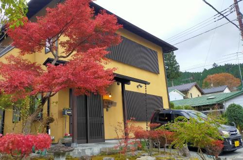 una casa gialla con alberi rossi di fronte di Guest House Koundo a Nikko