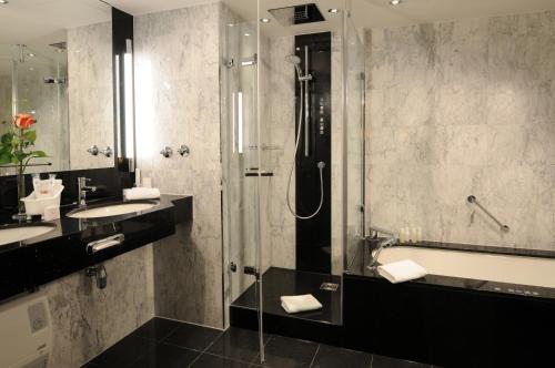 a bathroom with a shower and a sink and a tub at Maritim Hotel München in Munich