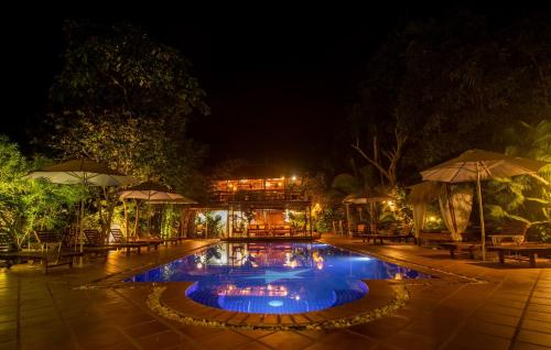 a swimming pool at night with tables and umbrellas at TARA LODGE Haven of peace in Kep