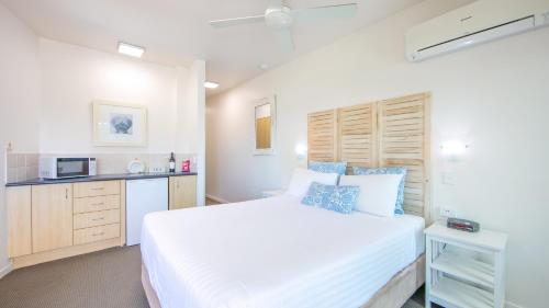a bedroom with a large white bed and a kitchen at Yamba Beach Motel in Yamba