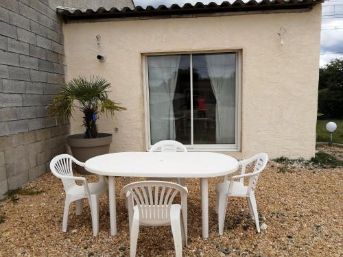 une table et des chaises blanches devant une fenêtre dans l'établissement La Petite Maison Des Vignes, à Les Églisottes-et-Chalaures