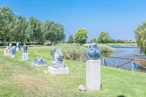 a group of statues sitting on the grass next to a river at Pini Village Lido Altanea in Caorle