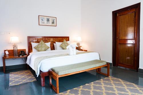 a bedroom with a large white bed with a bench at Saraca Resort & Spa Corbett in Garjia