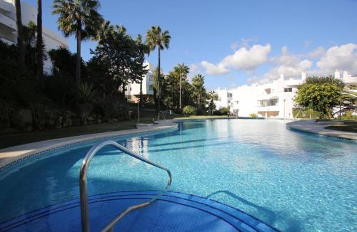 a large blue swimming pool with palm trees and a building at Estepona Golf Apartment in Estepona