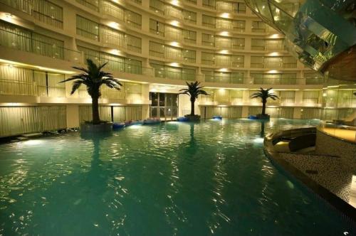 a large swimming pool with palm trees in a building at Royal treats at Rajhans Belliza Near Airport in Surat