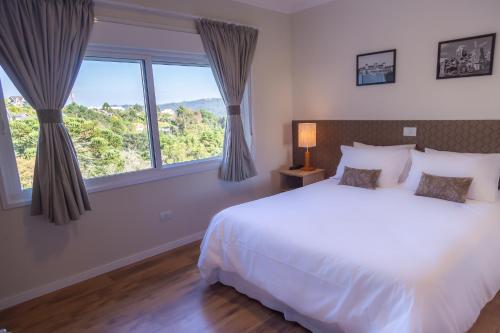 a bedroom with a white bed and large windows at Village de Charme - 2km do Capivari in Campos do Jordão