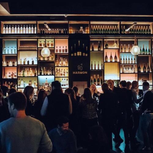 una multitud de personas en un bar con botellas de vino en Harmon House, en Bruselas