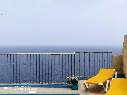 a yellow chair on a balcony with a view of the ocean at 3 bedrooms villa with private pool and wifi at Qala in Qala