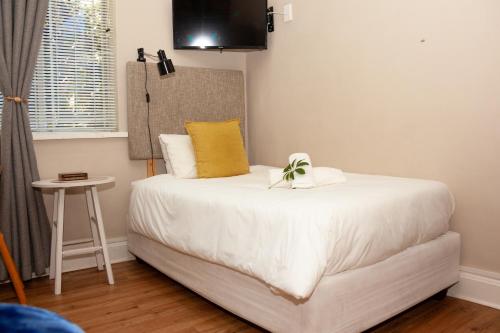 a bedroom with a white bed with a yellow pillow at De Akker Guest House Oudtshoorn in Oudtshoorn