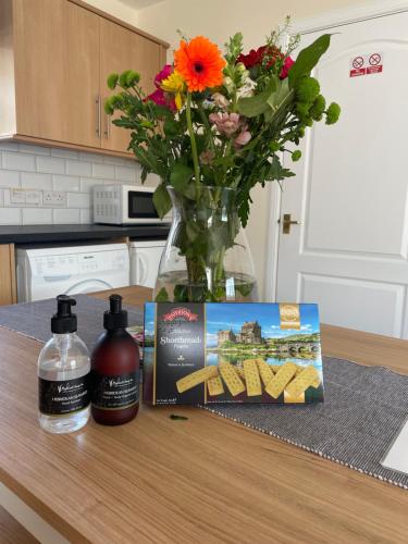 una mesa con un jarrón de flores y una botella de productos para el pelo en Ramblers Rest Modern Cottage-Perfect Views of Ben Nevis, en Fort William