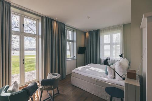 a bedroom with a bed and some chairs and windows at Hotel Strandleben in Schleswig