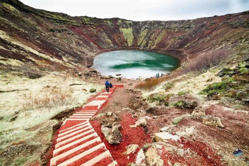 a person walking down a path in a quarry with a green lake at EYVÍK Cottages - Private HOT TUB! in Selfoss