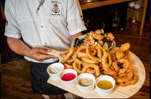 a man holding a tray of onion rings and onion rings at Hotel and Dive Center Roatan Yacht Club in Roatán