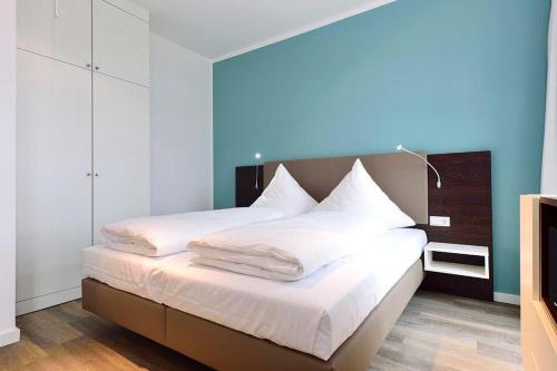 a bedroom with a bed with white sheets and a blue wall at Aparthotel Anna Düne Aparthotel Anna Düne 2-40 in Wangerooge