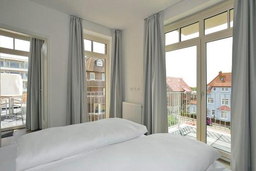 a white bedroom with a bed and large windows at Aparthotel Anna Düne Aparthotel Anna Düne 2-39 in Wangerooge