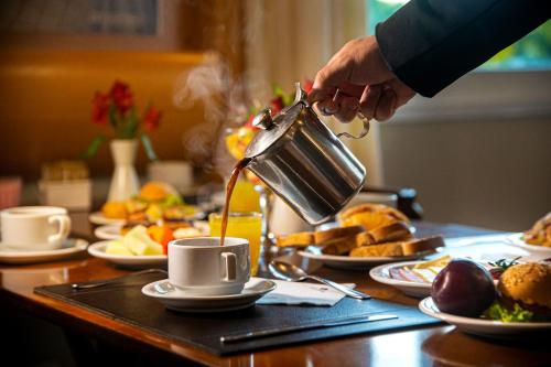 una persona che versa il caffè in una tazza su un tavolo di Hotel Laghetto Siena Gramado a Gramado