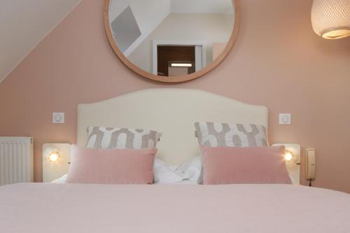 a white bed with pink pillows and a mirror at Les Chants d'Ailes - Hôtel Face Mer in La Turballe