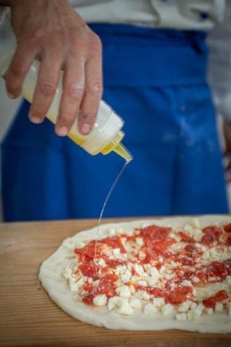 a person is pouring sauce on a pizza at Casale Guarracino in Sant'Agnello
