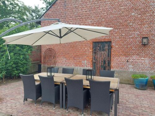 einem Holztisch mit Stühlen und einem weißen Regenschirm in der Unterkunft De Beredoezen - sfeervolle vakantiewoning in de gezellige Kempen in Retie