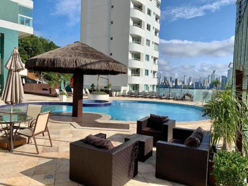 - une piscine avec des chaises, une table et un parasol dans l'établissement Cobertura Melhor Vista do Mar Balneário Camboriú, à Balneário Camboriú