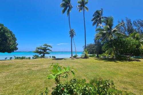 a grassy field with palm trees and the ocean at Villa Tiarenui in Maharepa