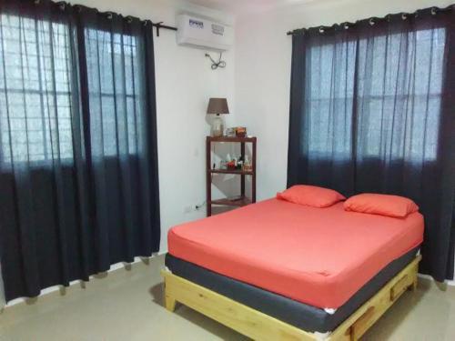 a bedroom with a bed with red sheets and black curtains at Bright Apartment at Punta Cana WIFIAcElectIronParking in Punta Cana