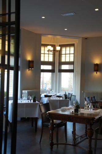 a restaurant with white tables and chairs and windows at Grand Hotel Belle Vue in De Haan